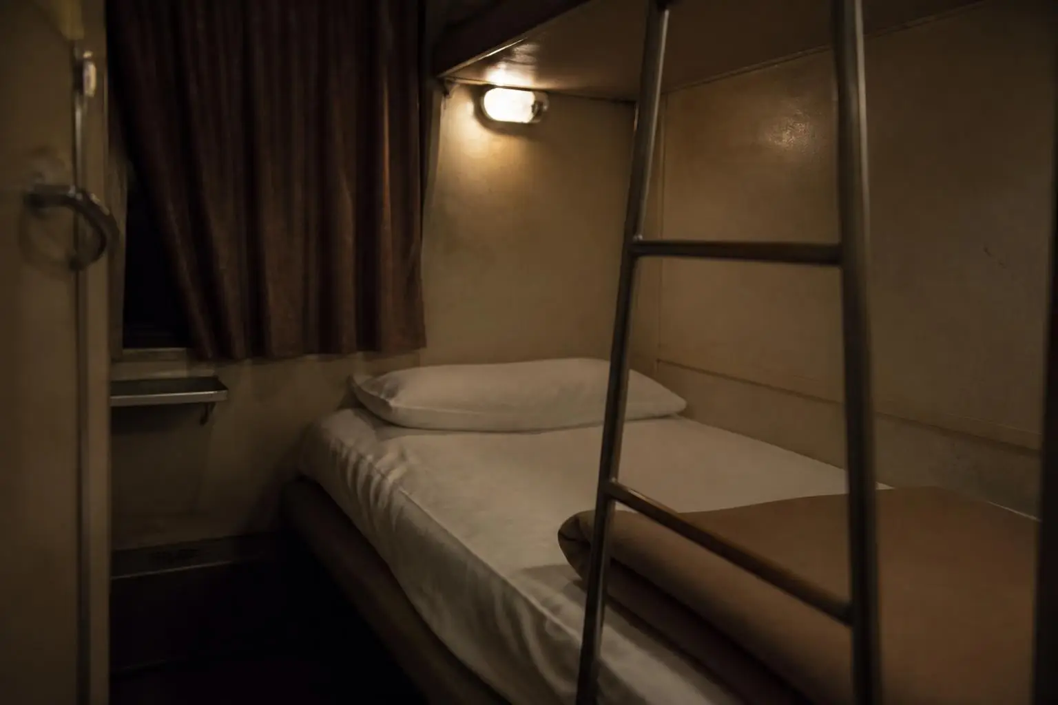Couchette basse d'un compartiment de train de nuit, rideau tiré sur la vitre et veilleuse allumée