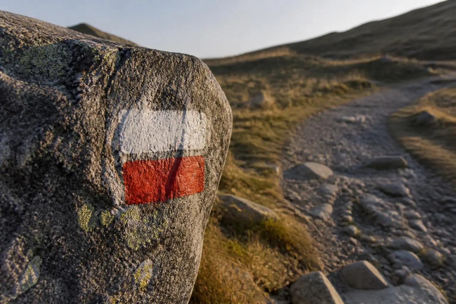 Balise de grande randonnée peinte en blanc et rouge sur un bloc de granit, au bord d'un sentier de pierres